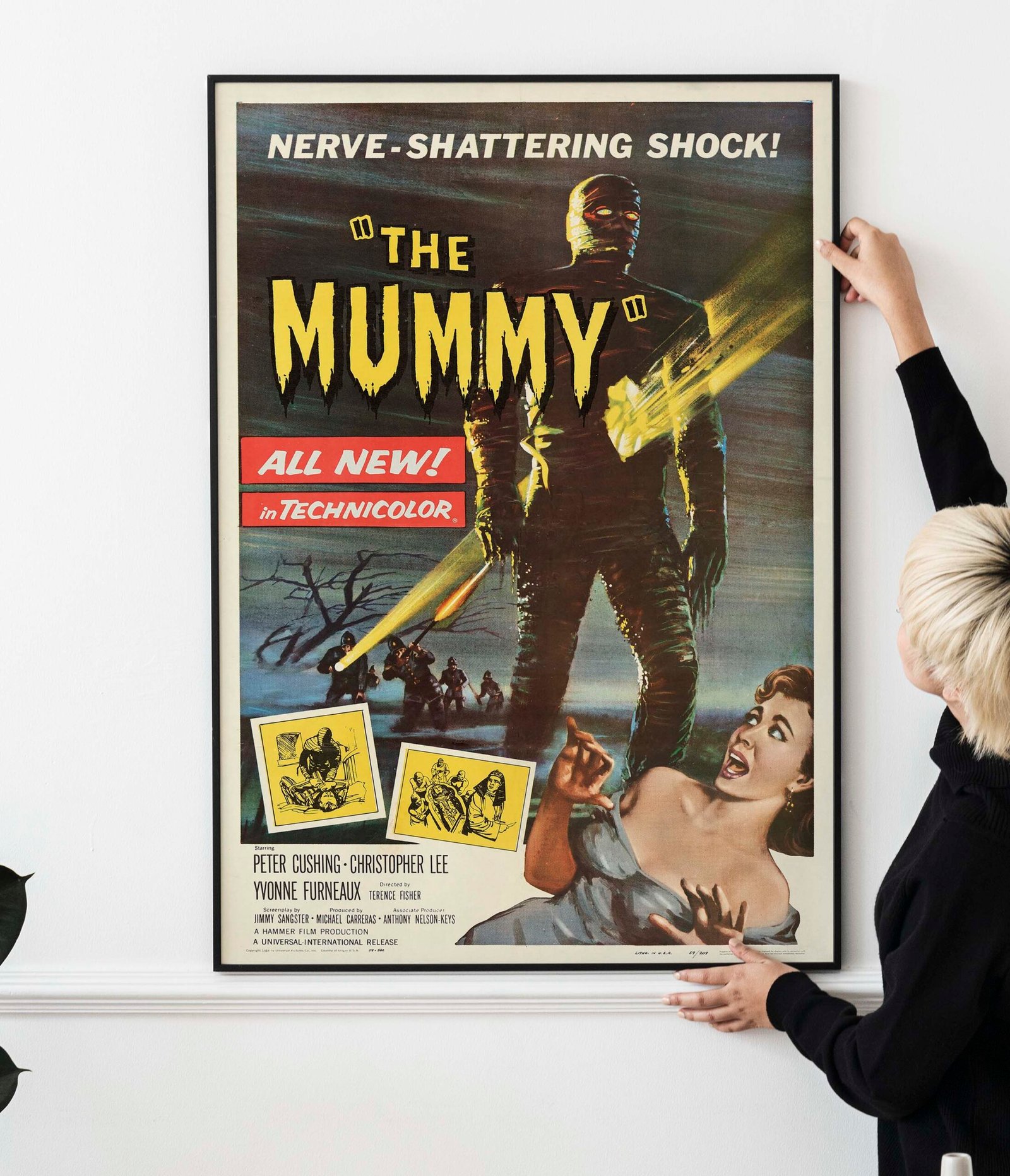 Blond haired Asian woman hanging a frame mockup on a white wall