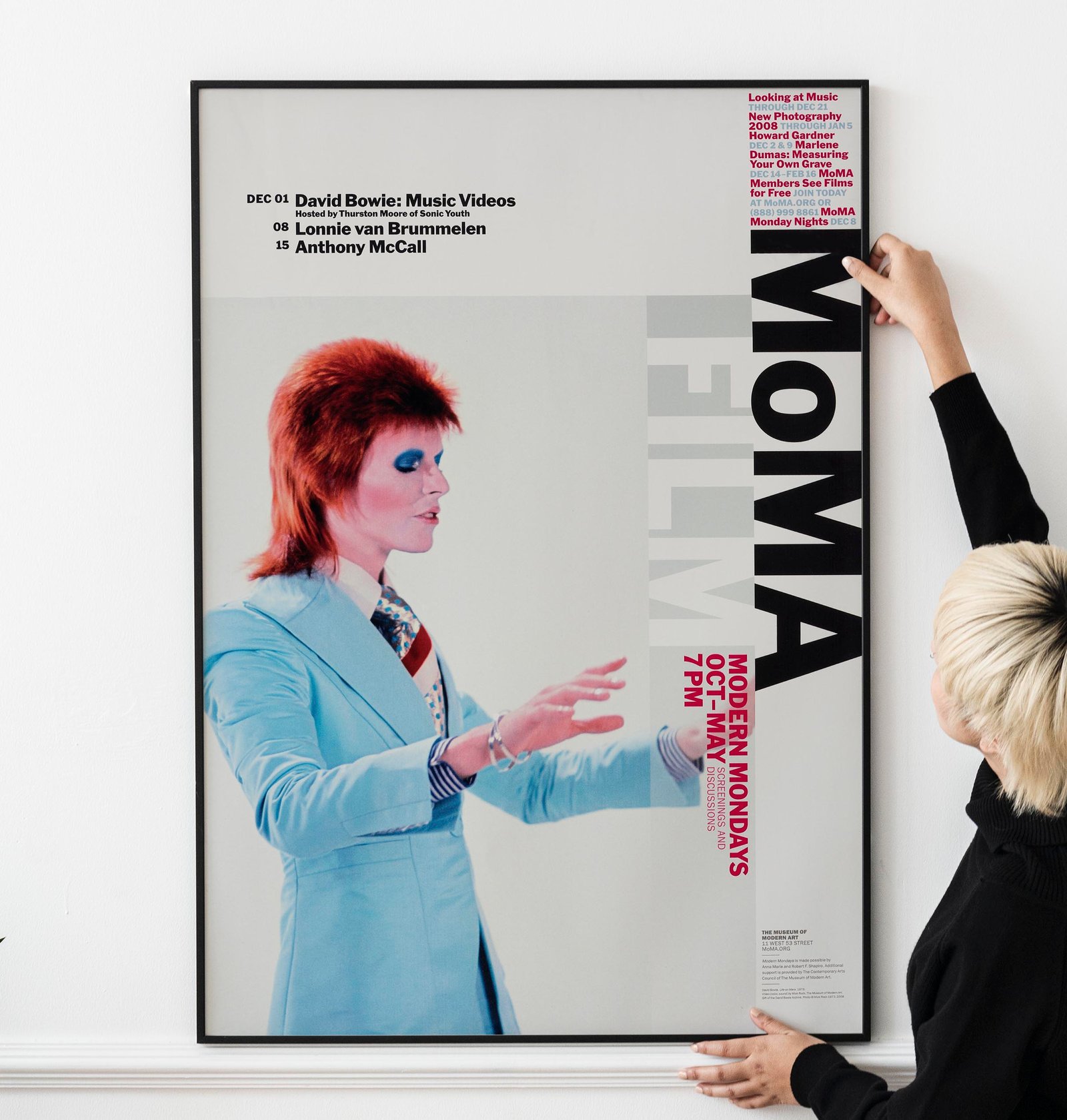 Blond haired Asian woman hanging a frame mockup on a white wall